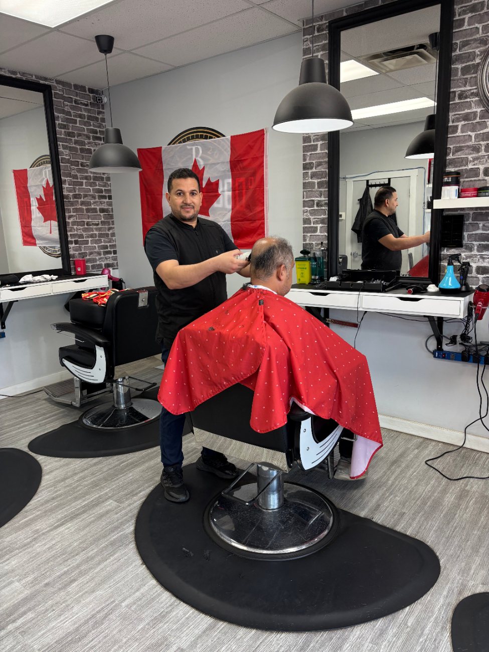 A Capilano Barbershop barber smiling while cutting a client's hair