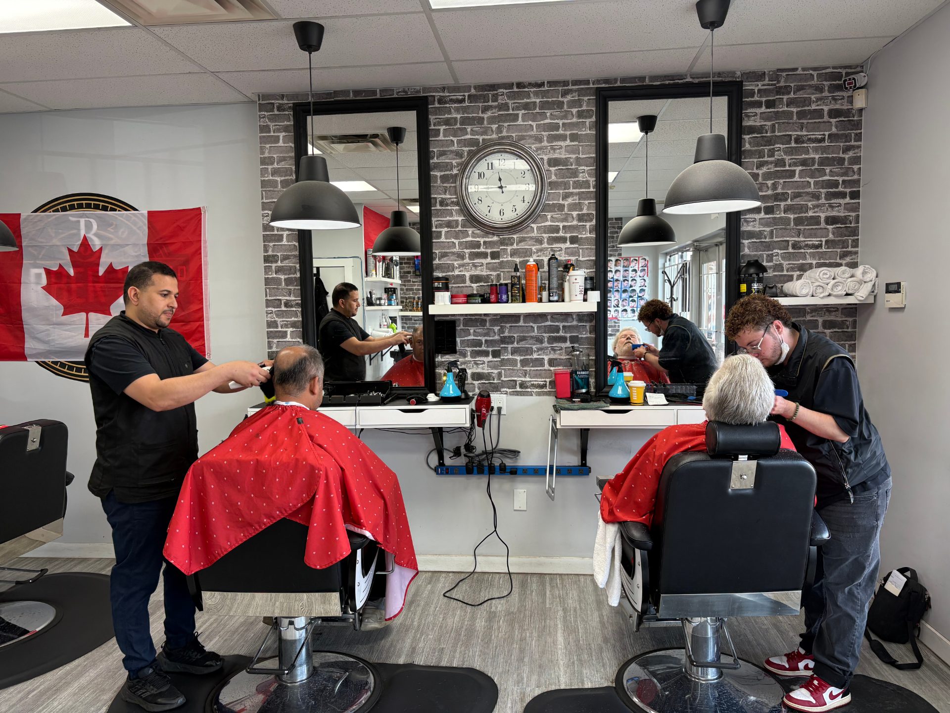 Two barbers cutting clients' hair inside Capilano Barbershop